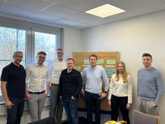 Personengruppe stehend vor einer befüllten Workshop-Pinnwand.