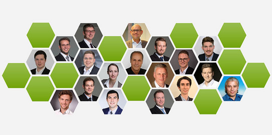 Das Bild zeigt eine Kollage von Porträtfotos mehrerer Personen, die in einer hexagonalen (sechseckigen) Anordnung dargestellt sind. Insgesamt sind 21 Personen zu sehen, darunter Männer und eine Frau, die alle in professioneller Kleidung abgebildet sind. Die Hexagone mit den Porträtfotos sind abwechselnd mit grünen, leeren Hexagonen angeordnet, die ein gleichmäßiges Muster bilden. Die Anordnung und die professionelle Darstellung der Personen deuten darauf hin, dass es sich um Mitglieder eines Teams oder einer Organisation handelt.