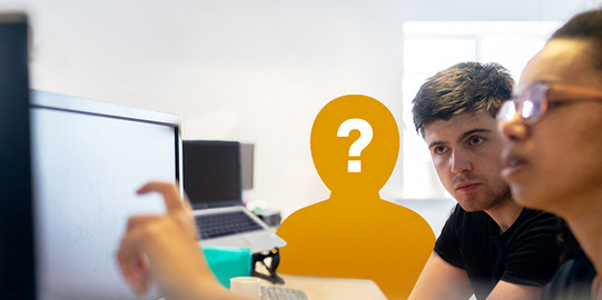Zwei Personen sitzen am Schreibtisch und schauen auf den Bildschirm. Im Hintergrund die orangene Silhouette einer dritten Person mit Fragezeichen im Gesicht.