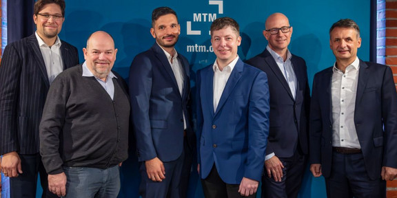 Sechs Personen stehen vor dem MTM-Logo.