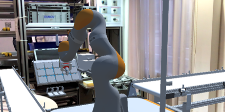 Foto eines modernen industriellen Arbeitsplatzes mit einem grauen Roboterarm, der orangefarbene Akzente hat. Der Roboterarm befindet sich in der Mitte des Bildes auf einer Arbeitsfläche und ist umgeben von verschiedenen technischen Geräten und Regalen mit Bauteilen. Im Hintergrund sind weitere industrielle Komponenten und eine Arbeitsumgebung zu sehen. Der Raum ist gut beleuchtet und wirkt technisch fortschrittlich. Links unten im Bild ist ein Bildschirm mit der Aufschrift "Hauptmenü" zu erkennen.