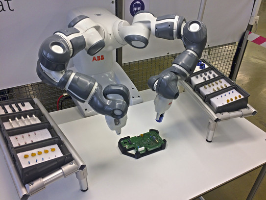 Zweiarmiger Roboter platziert THT-Bauteile auf Platine. Auf beiden Seiten liegen weitere THT-Bauelemente vereinzelt bereit.