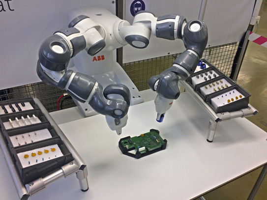 Zweiarmiger Roboter platziert THT-Bauteile auf Platine. Auf beiden Seiten liegen weitere THT-Bauelemente vereinzelt bereit.