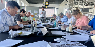 Auf dem Bild sind die Teilnehmer im Workshop zu sehen. Sie Falten Papierflieger im Werkbankprinzip.