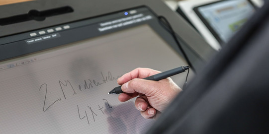 Writing at the lecture hall desk Screen of a lecture hall desk where someone is writing with a pen in hand.