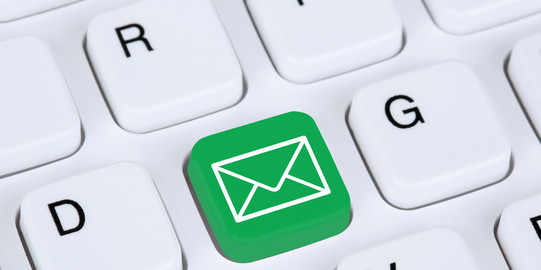 Email Eine weiße Tastatur im Detail. Eine Taste ist grün eingefärbt mit einem weißen Briefumschlag darauf.