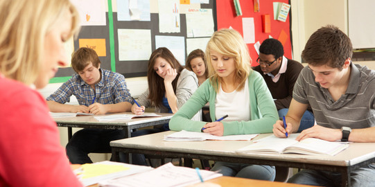 Classroom teaching Pupils sit in a class and write in notebooks sitting in front of them a teacher at a desk.