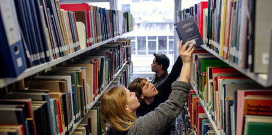 Studierende suchen nach Büchern in Bücherregalen in der Bibliothek.