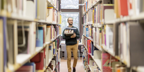 Student walks along the bookshelves in the library.