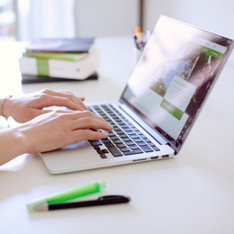 Studentin tippend am Laptop, daneben liegen Bücher und Stifte.